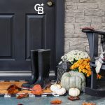 Traditional style front porch decorated for autumn with rain boots, heirloom gourds,  white pumpkins, mums and rocking chair with buffalo plaid pillow and throw blanket giving an inviting atmosphere.