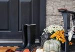 Traditional style front porch decorated for autumn with rain boots, heirloom gourds,  white pumpkins, mums and rocking chair with buffalo plaid pillow and throw blanket giving an inviting atmosphere.